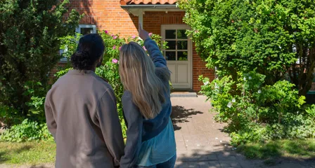 Par står foran murstensvilla med hvid dør og peger